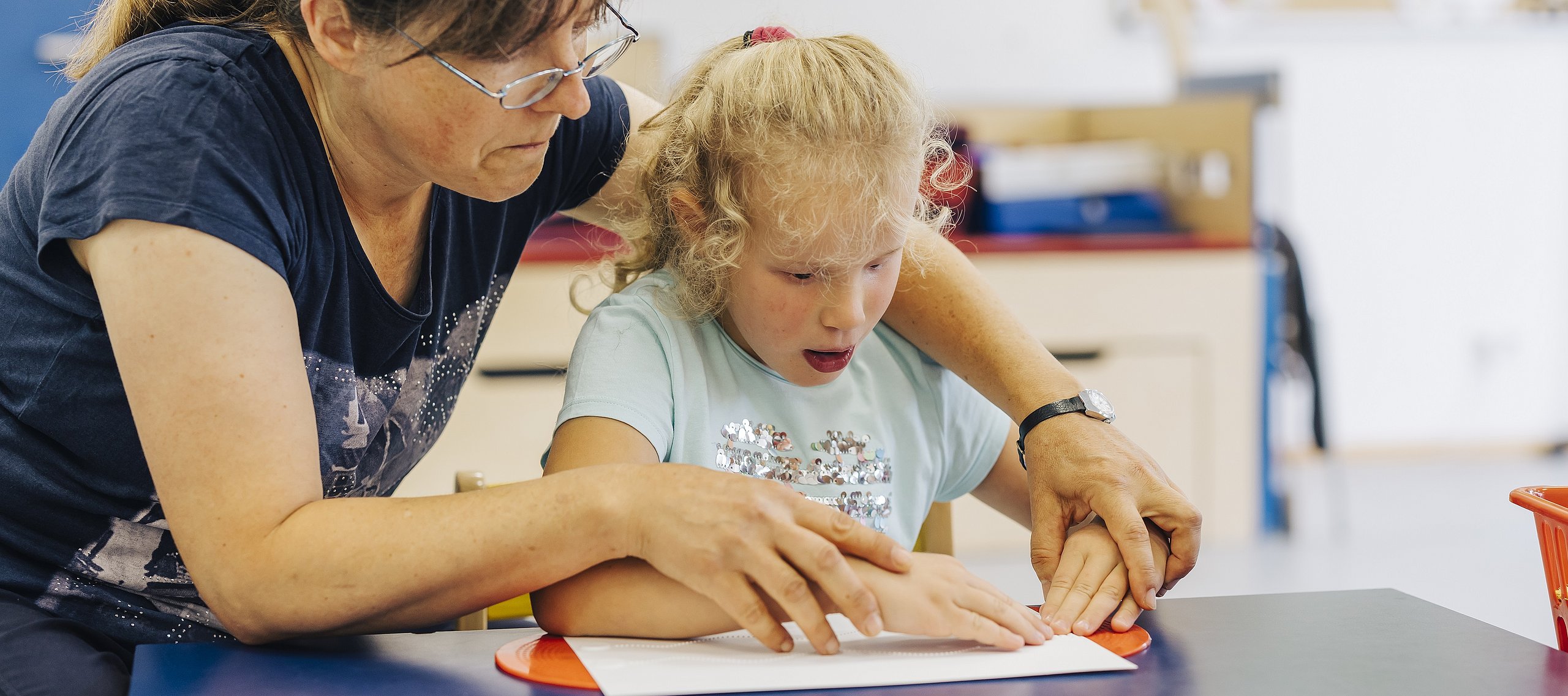 Eine junge Schülerin ertastet mit Hilfe ihrer Lehrerin einen Text in Brailleschrift.